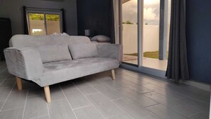 Un sofá gris en una sala de estar moderna, con un amplio ventanal corredero que da a un espacio exterior.