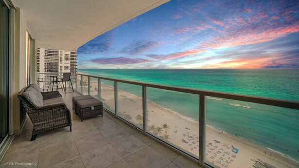 A balcony with wicker furniture overlooking a beach and ocean during sunset. - Balcony on the Ocean Picture Perfect (Sunny Isles Beach)