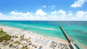 A beach with a pier extending into the ocean, rows of beach chairs, and umbrellas. - Balcony on the Ocean Picture Perfect (Sunny Isles Beach)