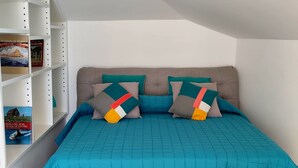 Un dormitorio con colcha color turquesa, cabecera y estantería llena de libros.