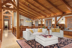 A spacious living area with high ceilings and exposed wooden beams, featuring two white sofas with yellow cushions, a coffee table, and a patterned rug. - Bainbridge Is waterfront lodge w private beach access and extensive amenities (Bainbridge Island)