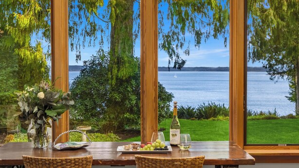 Uma mesa de jantar com vista para um lago, uma garrafa de vinho e um prato de frutas.