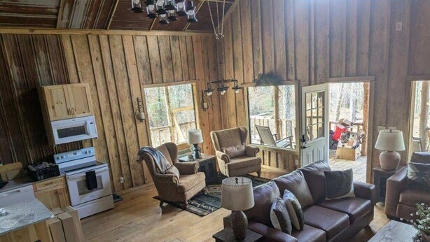 A rustic cabin interior with wooden walls, a dining area, a sofa, and a kitchen with a microwave and stove.