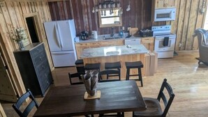 A wooden interior with a dining table, chairs, a refrigerator, a stove, and a sink.