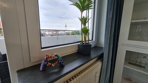 A room with a large window overlooking a cityscape, including a tower. A potted plant is on the windowsill, and a colorful item is on the countertop. - DEICHLIEBE 1 - fantastic view, own garage & contactless check-in (Bremerhaven)