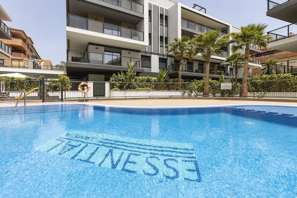 A modern building with balconies, a swimming pool, and palm trees.