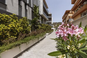 Um caminho ladeado por edifícios modernos com varandas, uma construção baixa e vegetação exuberante.