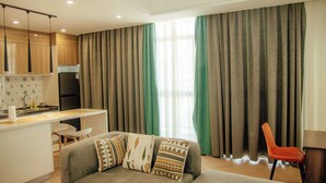A modern living room with a sofa, a dining area with a kitchen in the background, and a large window with curtains. - 1 bedroom spacious, modern and cozy apartment nestled in upperhill nairobi Kenya (Nairobi)