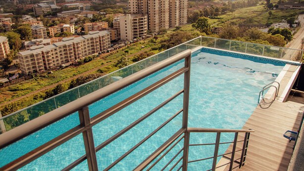 A rooftop infinity pool with a glass barrier, offering a view of surrounding buildings and greenery. - 1 bedroom spacious, modern and cozy apartment nestled in upperhill nairobi Kenya (Nairobi)