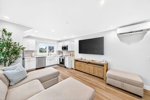 Una cocina moderna con armarios blancos, un ventanal grande y un televisor de pantalla plana montado en la pared.