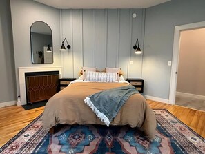 A bedroom with a large bed, a patterned rug, a mirror, and two wall-mounted lamps. - Wander & Wonder: A Hidden Gem in Portland’s Heart (Portland)