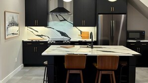A modern kitchen with black cabinets, a central island, and pendant lighting. - Wander & Wonder: A Hidden Gem in Portland’s Heart (Portland)
