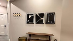 A hallway with a wooden floor, a coat rack, three framed abstract artworks, a wooden bench, and a wicker basket. - Wander & Wonder: A Hidden Gem in Portland’s Heart (Portland)