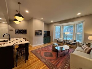 A modern living room with a kitchen area, large windows, and a cozy seating arrangement. - Wander & Wonder: A Hidden Gem in Portland’s Heart (Portland)