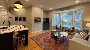 A modern living room with a kitchen area, large windows, and a cozy seating arrangement. - Wander & Wonder: A Hidden Gem in Portland’s Heart (Portland)