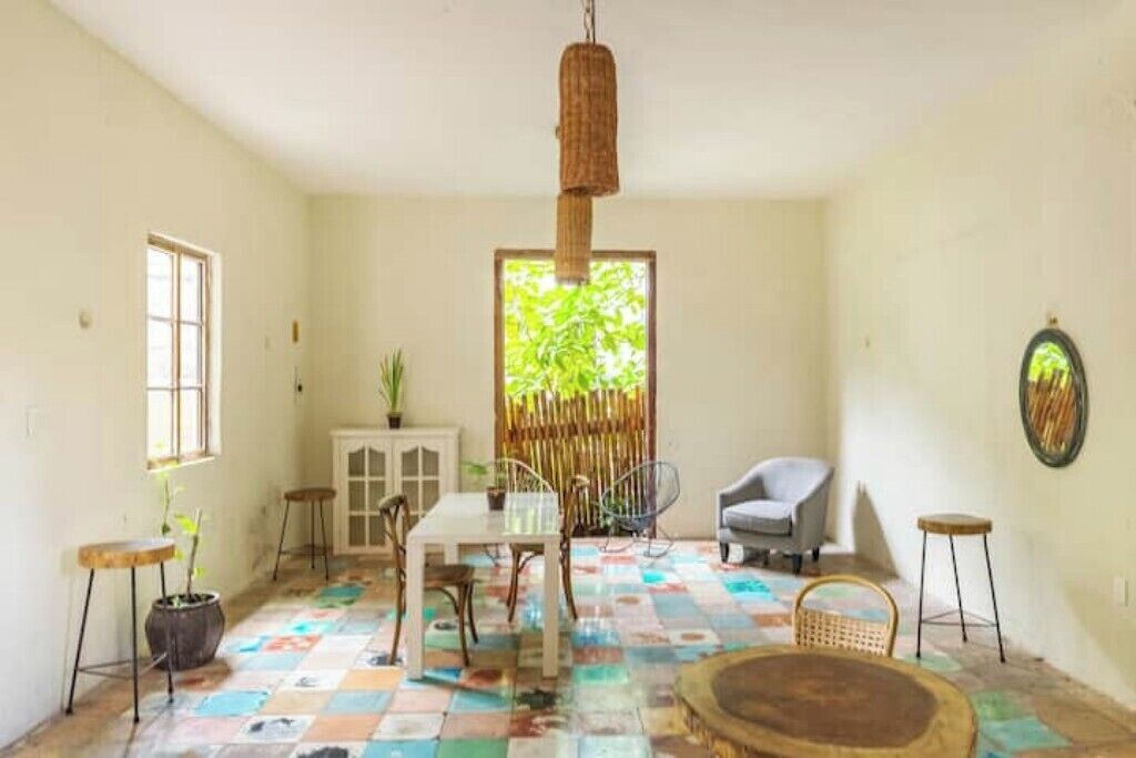 Une pièce avec un sol à carreaux, une table à manger avec des chaises, un luminaire suspendu, une fenêtre et une plante.