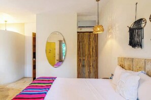 Une chambre à coucher comprenant un lit, un miroir, un luminaire suspendu et une décoration murale en macramé.
