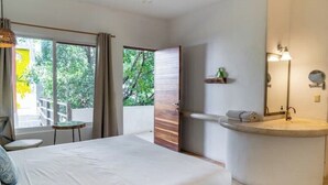 Ein modernes Hotelzimmer mit einem großen Bett, einem Badezimmer mit einem runden Waschbecken und Blick auf Grünflächen.