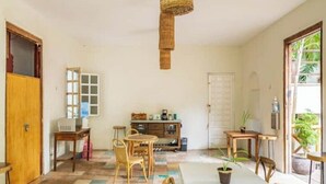 Ein Zimmer mit gefliestem Boden, einem Esstisch mit Stühlen, einer Küchenzeile mit Herd und einem Fenster mit Blick ins Grüne.