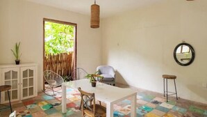 Ein Zimmer mit einem weißen Tisch, zwei Stühlen, einem kleinen Hocker, einer Schrank mit Glastüren, einem hängenden Korb und einem Spiegel an der Wand.