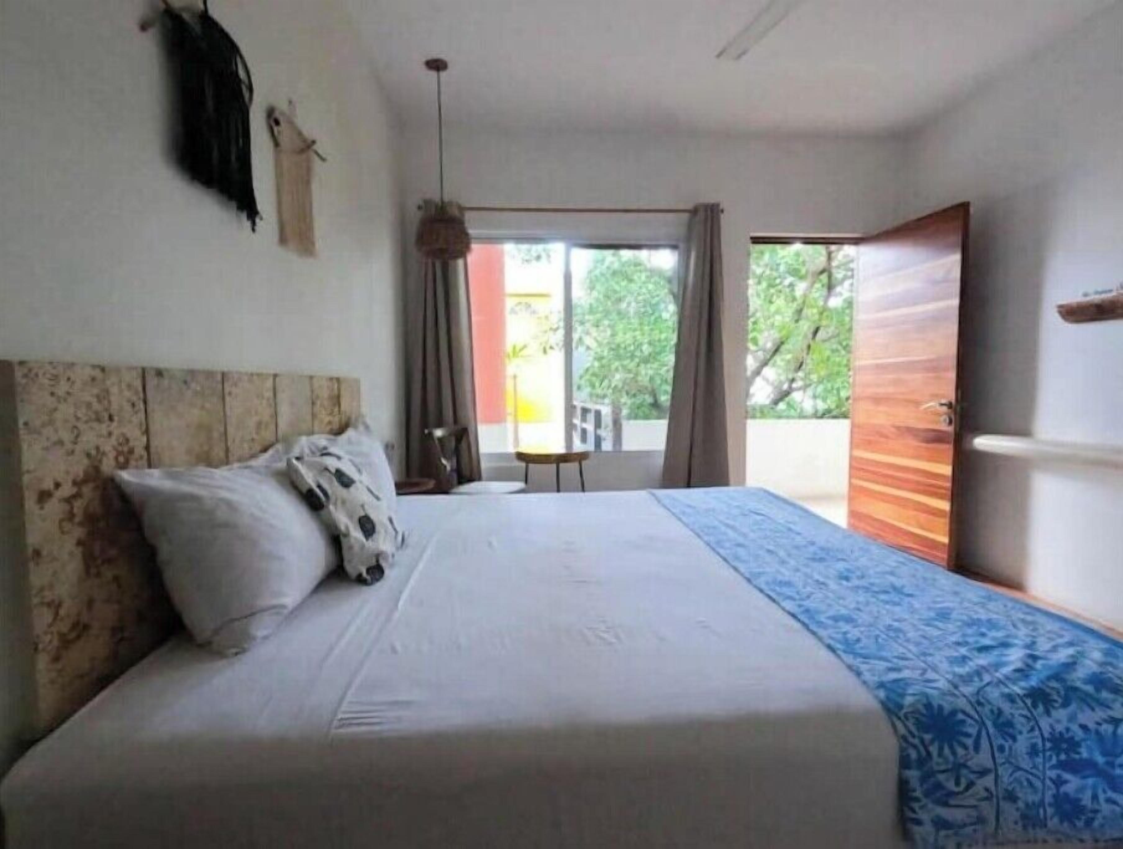 Quarto com cama, uma mesinha e vista para o exterior.