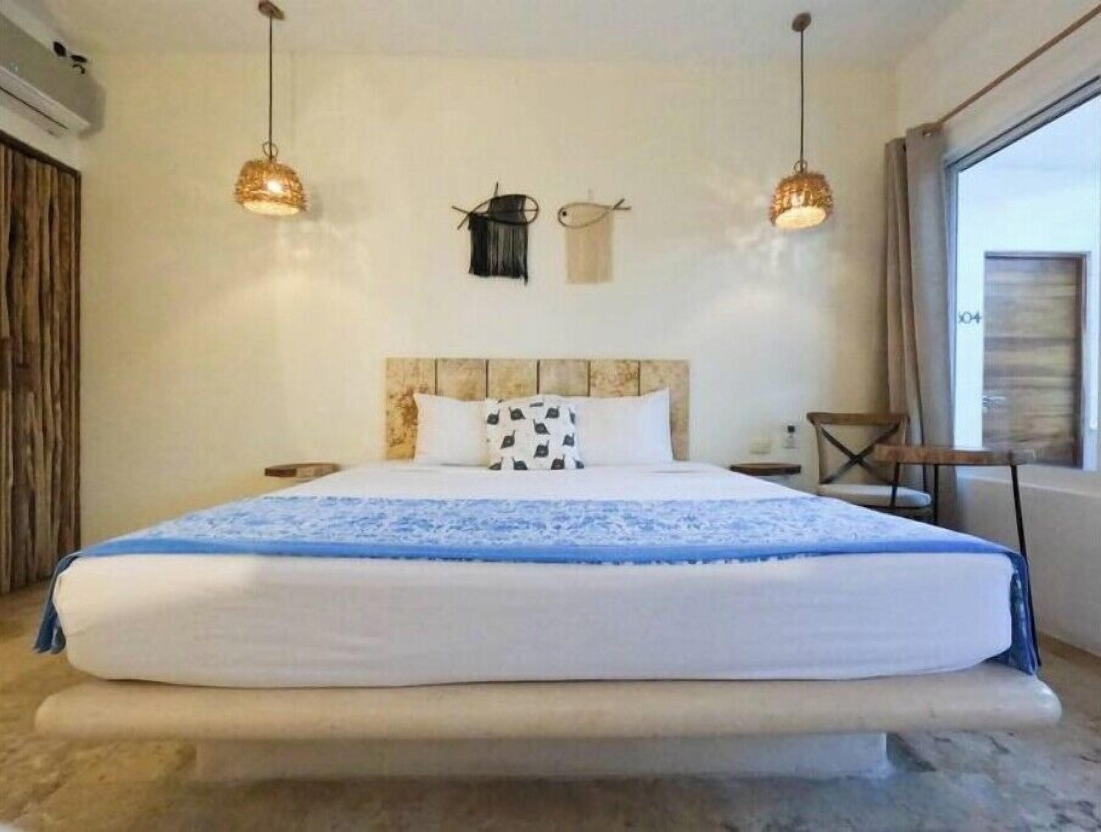 Een groot bed met hoofdeinde, twee hangende lampen, een nachtkastje en een raam met gordijnen.