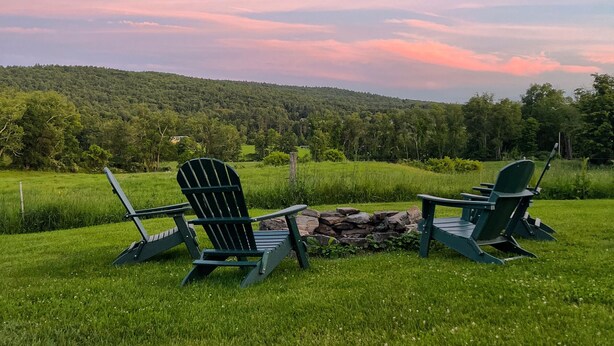 Two Adirondack chairs and a fire pit in a grassy field with a forested hill in the background. - Large Farmhouse with expansive views, firepit 15 min north of Keene (Walpole)