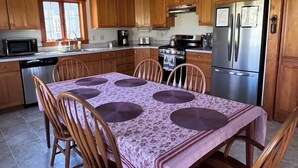 A kitchen with wooden cabinets, a dining table with chairs, a chandelier, and modern appliances. - Large Farmhouse with expansive views, firepit 15 min north of Keene (Walpole)