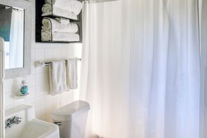 Een badkamer met toilet, wastafel en een spiegel boven de wastafel. Handdoeken hangen aan een rek en er is een douchegordijn.