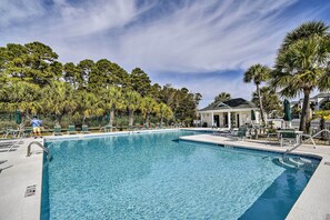 Une piscine d’un bleu éclatant, entourée de chaises longues et de palmiers, avec un bâtiment en arrière-plan.