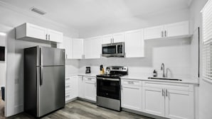 A modern kitchen with white cabinets, stainless steel appliances, and a wooden floor. - The Heights Collective (Tampa)