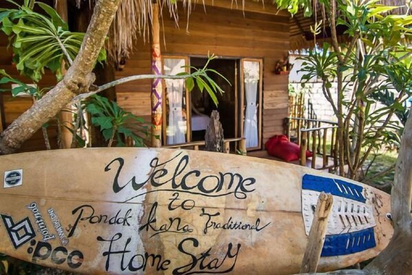 A wooden boat with 'Welcome to Pondok Rani Traditional Home Stay' written on it, parked in front of a rustic wooden building.