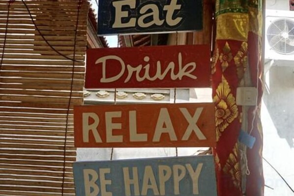 A wall with multiple signs, including 'Eat,' 'Drink,' 'RELAX,' and 'BE HAPPY.' - Pondok Kana and Hostel by Ecommerceloka (Bali)