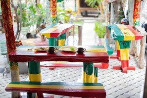 Mesas al aire libre con patas pintadas de colores y piso de baldosas.