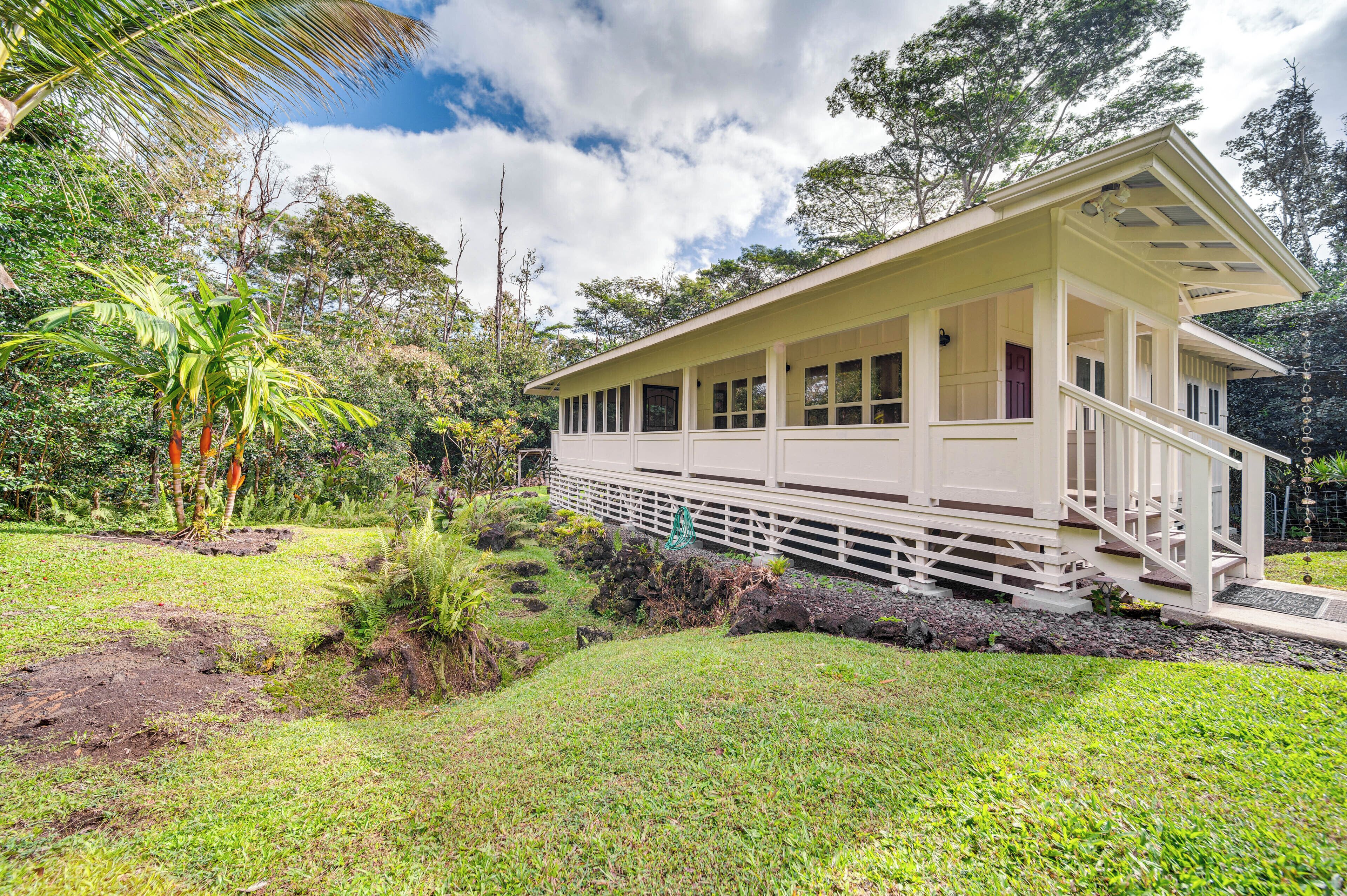 A single-story house with a porch, surrounded by lush greenery and trees.