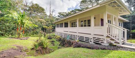 A single-story house with a porch, surrounded by lush greenery and trees.