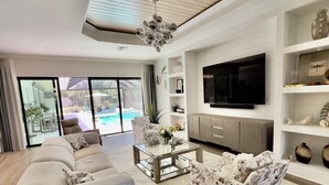 A modern living room with a sofa, armchair, coffee table, and TV. - Estate Bungalow With TPC golf course. Luxury, in and out. (Naples)