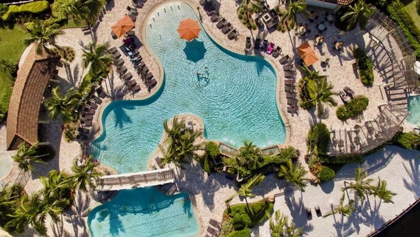 An aerial view of a resort with a central swimming pool, sun loungers, palm trees, and a bridge. - Estate Bungalow With TPC golf course. Luxury, in and out. (Naples)