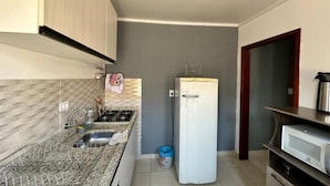 Una cocina compacta con encimera de granito, pileta integrada, refrigerador blanco y microondas sobre una repisa de madera.