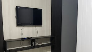 Una habitación con una televisión de pantalla plana montada en la pared, un mueble de entretenimiento negro debajo y piso de baldosas.