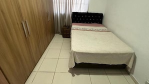 Un dormitorio pequeño y ordenado con una cama individual, un armario de madera y una cortina.