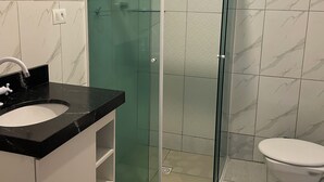 Un baño con ducha de vidrio, lavamanos con encimera negra y un inodoro.