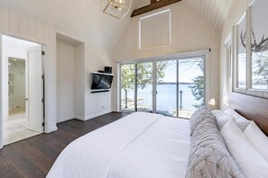 Een slaapkamer met een groot bed, een televisie en een schuifdeur met uitzicht op een meer.