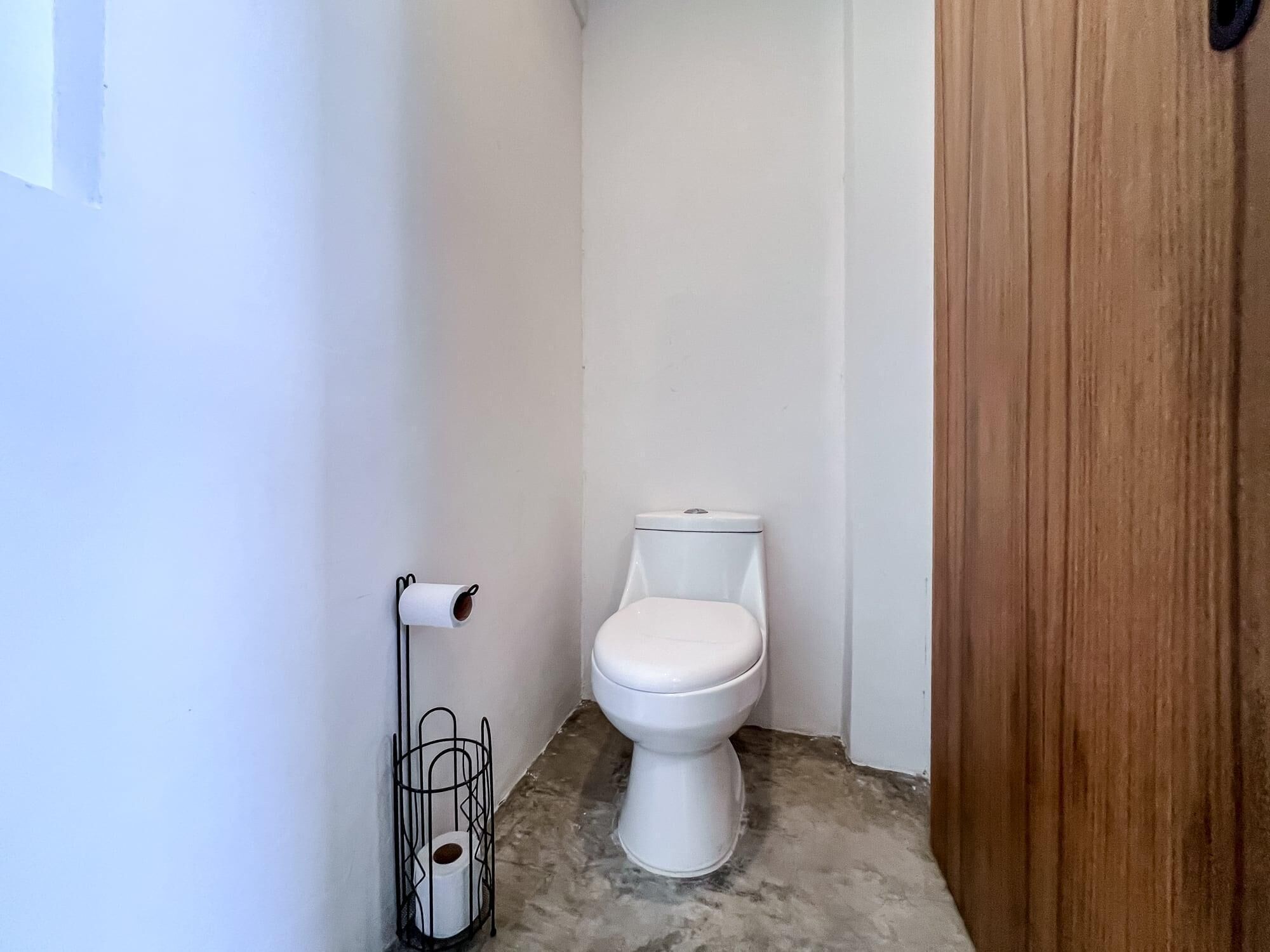 A small, clean bathroom with a white toilet, a toilet paper holder, and a metal rack.