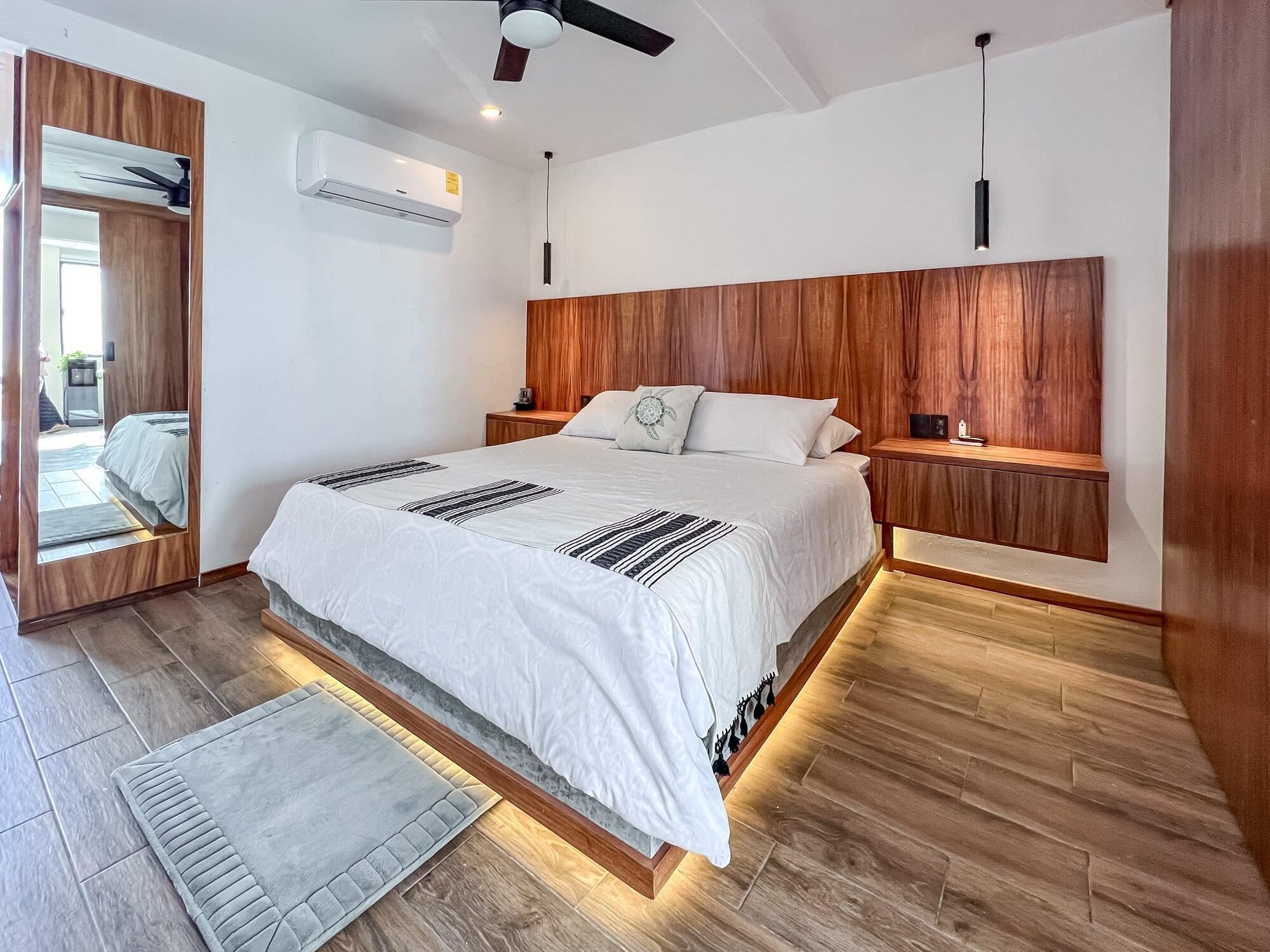 A modern bedroom with a large bed, wooden headboard, bedside tables, and a built-in bench.