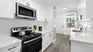 A modern kitchen with white cabinetry, a stainless steel stove, and a microwave. - The Heights Collective (Tampa)