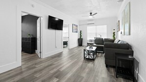 A modern living room with a grey sofa, a coffee table, and a fireplace. There is a flat-screen TV mounted on the wall and a ceiling fan. - The Heights Collective (Tampa)