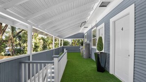A covered outdoor area with artificial grass, white railings, and a grey building with numbered doors. - The Heights Collective (Tampa)