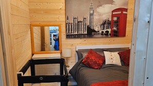 Un dormitorio acogedor con cama, espejo, cabecero de madera, pintura de una cabina telefónica roja y candelabro.