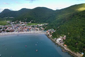 Vista aérea de uma vila costeira com praia, barcos e colinas verdejantes.
